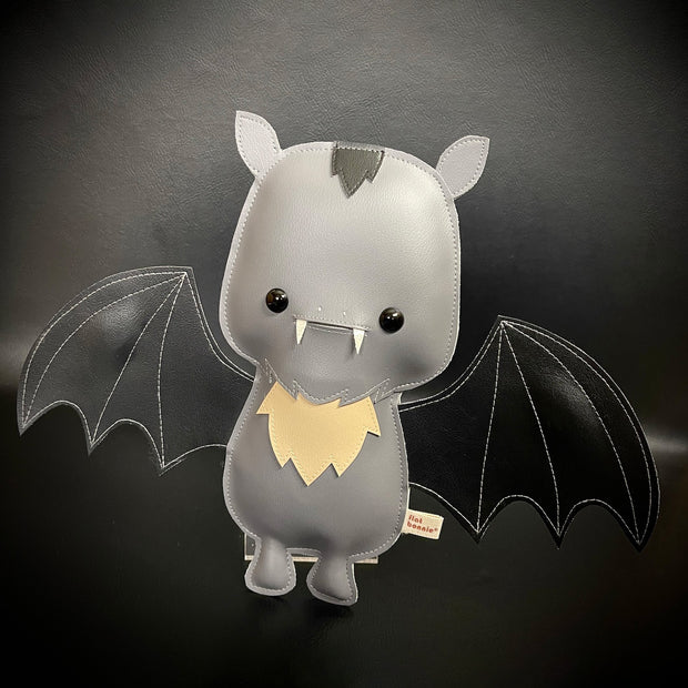 Vinyl plush of a cartoon style bat with small fangs and its wings spread out. 