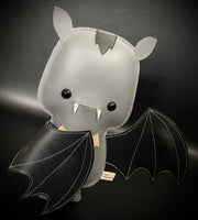 Vinyl plush of a cartoon style bat with small fangs and one of its wings pulled in towards its body.