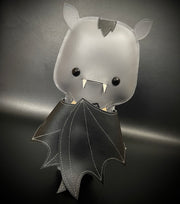 Vinyl plush of a cartoon style bat with small fangs and its wings pulled in towards its body.