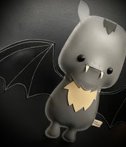 Vinyl plush of a cartoon style bat with small fangs and its wings spread out.