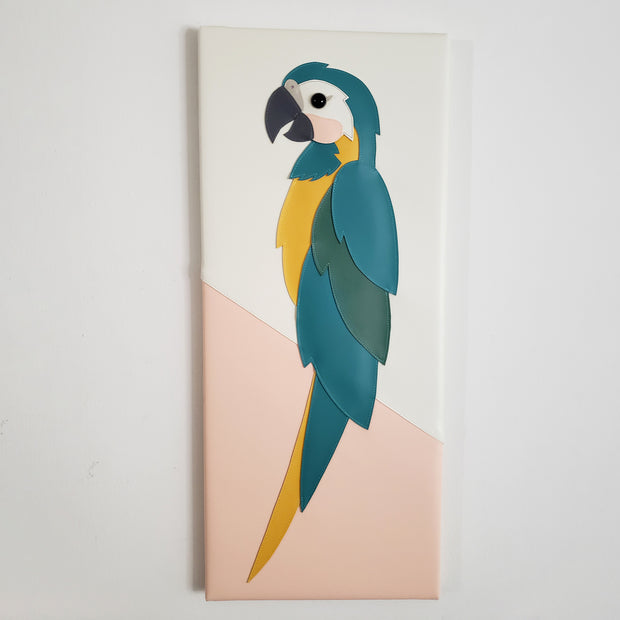 Vinyl canvas flat sculpture of a cartoon style blue throated macaw, facing to the left. It is on a vertical rectangle canvas, white with pink accent.