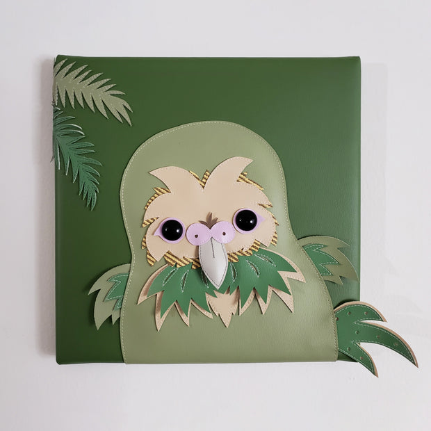 Vinyl fabric sculpture on a flat green square canvas of a cartoon style kakpo, with its beak flat from looking head on.