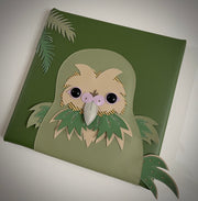 Vinyl fabric sculpture on a flat green square canvas of a cartoon style kakpo, with its beak flat from looking head on.