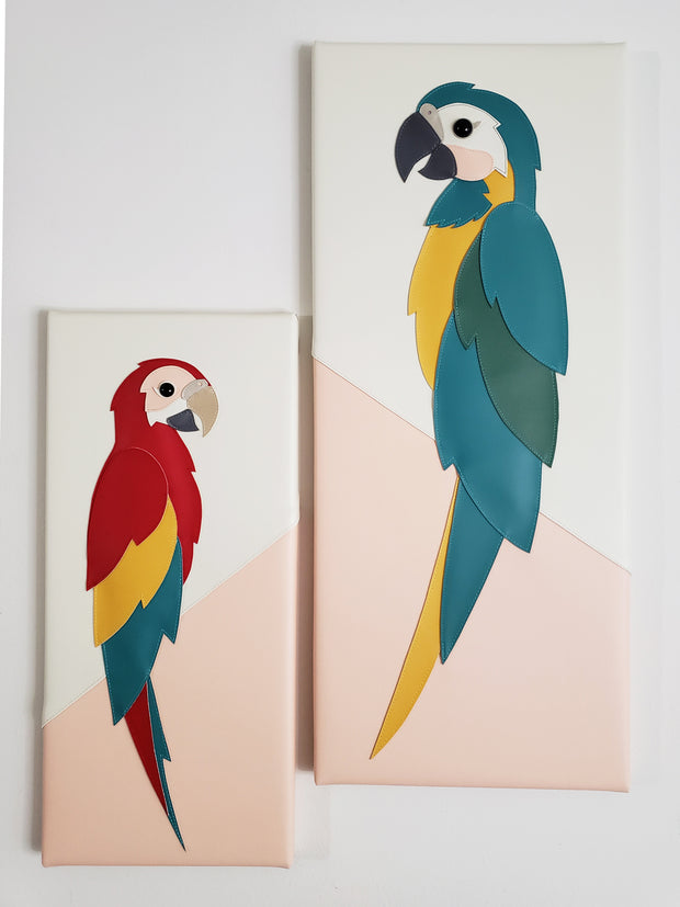 2 flat vinyl fabric sculptures on vertical rectangular canvases. One is of a flat blue throated macaw, facing to the right and the other is of a parrot, facing to the left.