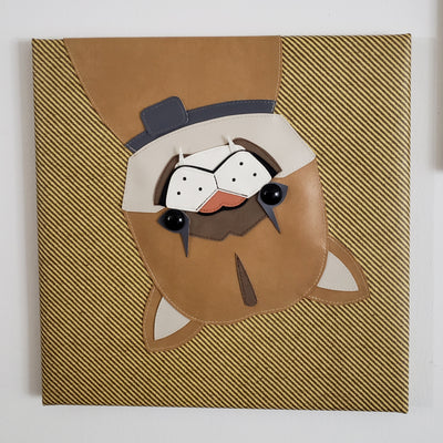Vinyl fabric sculpture on a flat striped tan square canvas of a cartoon style baby mountain lion, upside down with only its upper body visible.