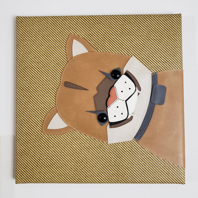 Vinyl fabric sculpture on a flat striped tan square canvas of a cartoon style baby mountain lion, appearing from the right of the canvas with only its upper body visible.