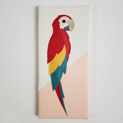 Vinyl canvas flat sculpture of a cartoon style scarlet macaw, facing to the right. It is on a vertical rectangle canvas, white with pink accent.
