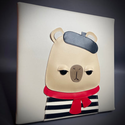 Artwork made of vinyl fabric on a flat vinyl canvas of a capybara looking unimpressed and wearing a beret, striped shirt and red scarf. 