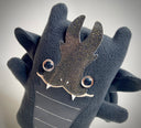 Black plush doll of a stylized dragon, with cute brown eyes and a ribbed stomach.