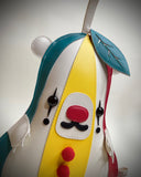 A flat, vinyl art plush of a pear designed like a bear dressed as a clown.