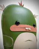 Vinyl fabric plush of a flat dinosaur/kaiju monster with a wide mouth and 2 buckteeth.