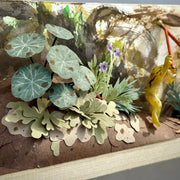 Close up detail shot of diorama style sculptural work, showing cut paper plants and leaves.