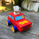 Toy truck with a dog figure on top, resembling Snoopy, on a wooden surface.