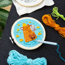 Embroidery hoop with a punch needle artwork of a capybara partially submerged in blue water with citrus fruits around it.