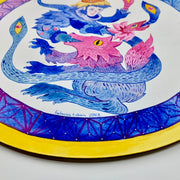 Bright blue and pink illustration on a circular panel with a yellow outline. A wolf creature is opens its mouth, a large blue snake creature comes out with a person's face.