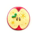 Flat backed sculpture of a red apple interior with small seeds and a tiny green worm coming out of it.