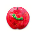 Flat backed sculpture of red apple with star patternings and a tiny green worm coming out of it.