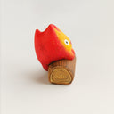 A small flame-shaped figurine with a red-to-orange gradient face and white eyes, sitting on a brown wooden log base against a plain light background.