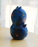 Sculpture of 2 cat heads, stacked atop of one another and painted to look like a night sky with shooting stars. Each head has a tiny, cute cat face and gold sparkly stars.