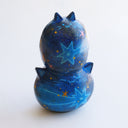 Sculpture of 2 cat heads, stacked atop of one another and painted to look like a night sky with shooting stars. Each head has a tiny, cute cat face and gold sparkly stars.