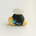 A small hand-painted figurine, the back view of a head with a white dog atop of it, decorated with blue and white star patterns, on a plain white background.