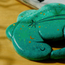 A painted clay sculpture of a sleeping dinosaur, curled into itself like a sleeping cat. It is a teal with stars painted and glitter stars pasted on.