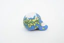 Ceramic sculpture of a blue planet with green floral dots, smiling and sitting next to a tiny moon.