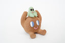 Sculpture of a brown, rounded character with legs sitting down. It holds a green smiling alien character atop its head.
