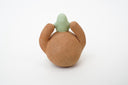 Sculpture of a brown, rounded character with legs sitting down. It holds a green smiling alien character atop its head.