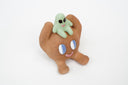 Sculpture of a brown, rounded character with legs sitting down. It holds a green smiling alien character atop its head.