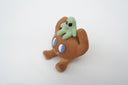 Sculpture of a brown, rounded character with legs sitting down. It holds a green smiling alien character atop its head.