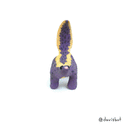 Ceramic sculpture of a purple skunk, done in a cartoon style with large bulbous black eyes and a very small, skinny head.