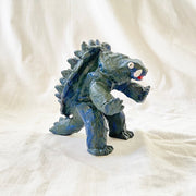 Stylistically messy sculpture of Gamera, a turtle monster with 2 large underbite fangs. It stands on 2 feet with its arms out in front of it. 