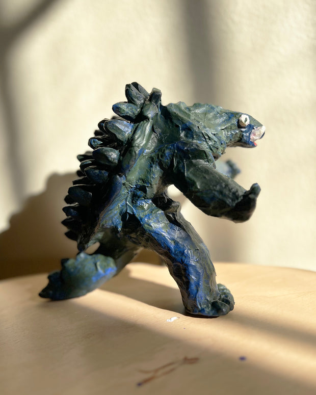Stylistically messy sculpture of Gamera, a turtle monster with 2 large underbite fangs. It stands on 2 feet with its arms out in front of it.