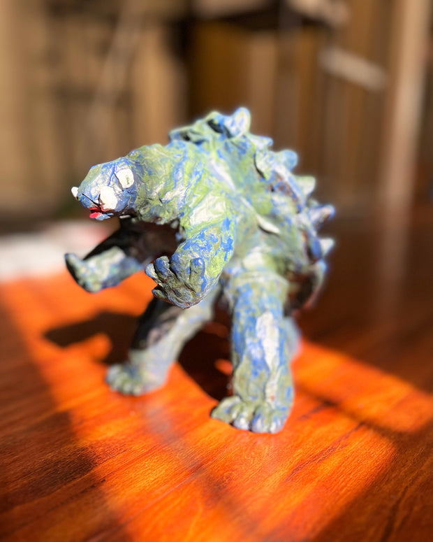 Stylistically messy sculpture of Gamera, a turtle monster with 2 large underbite fangs. It stands on 2 feet with its arms out in front of it.