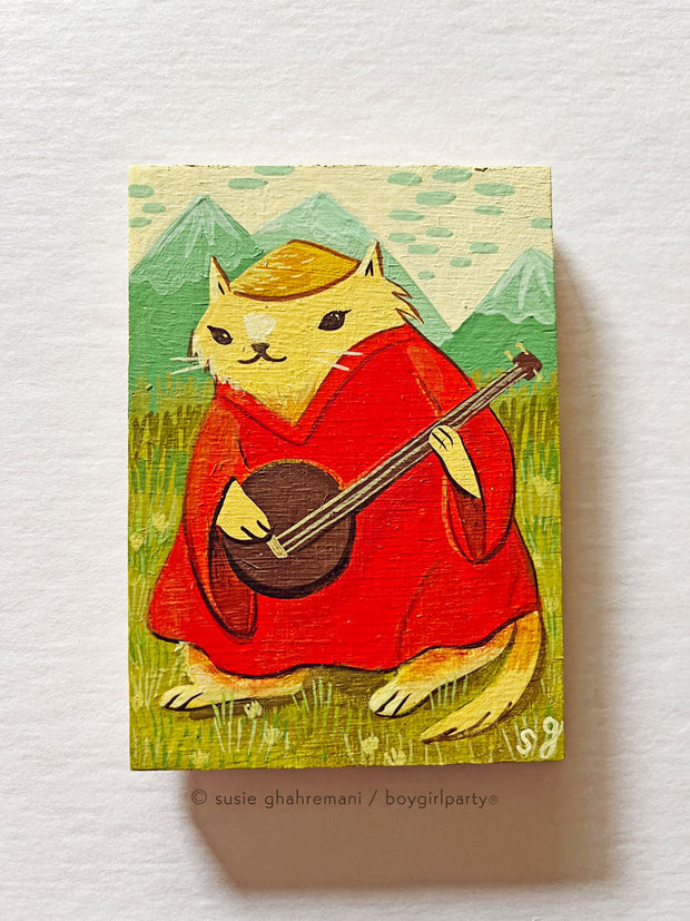 Painting of a chubby yellow cartoon cat in a red muumuu and straw hat, playing a 3 stringed instrument. It stands in an open field in front of tall green mountains.