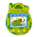 Clay sculpture of a handheld virtual pet toy with 3 buttons and a wording that reads "BogBuddy". It is green with darker green spots and on the "screen" is a frog eating flies.