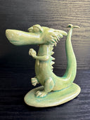 Jade colored ceramic sculpture of a dragon with a large front snout, positioned in a yoga pose with one leg up and its hands at its chest.