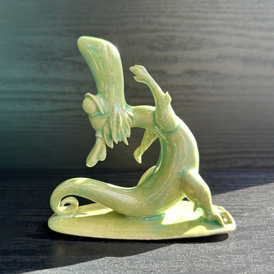 Jade colored ceramic sculpture of a dragon with a large front snout, positioned in a yoga pose with one leg in front of the other and its back bent, with one arm reaching up towards the sky.