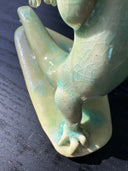 Jade colored ceramic sculpture of a dragon with a large front snout, positioned in a yoga pose with one leg in front of the other and its back bent, with one arm reaching up towards the sky.