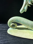 Jade colored ceramic sculpture of a dragon with a large front snout, positioned in a yoga pose with one leg in front of the other and its back bent, with one arm reaching up towards the sky.