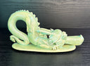 Jade colored ceramic sculpture of a dragon with a large front snout, positioned in the yoga stretch, child's pose.