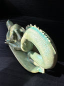 Jade colored ceramic sculpture of a dragon with a large front snout, positioned in the yoga stretch, child's pose.