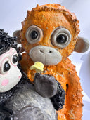 Two monkey figurines, one black and one orange, on a white background