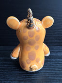 Ceramic figurine sculpture of an orange creature with mouse ears, a short but wide snout and 3 small horns coming out of the back of its head.