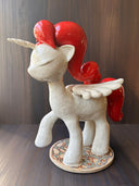 Ceramic unicorn figurine with red mane and tail on a wooden surface