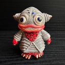 Ceramic figurine sculpture of a gray and red fish monster, with large yes and pointed ears. It has a large smile with sharp teeth.