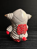 Ceramic figurine sculpture of a gray and red fish monster, with large yes and pointed ears. It has a large smile with sharp teeth.