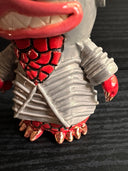 Ceramic figurine sculpture of a gray and red fish monster, with large yes and pointed ears. It has a large smile with sharp teeth.