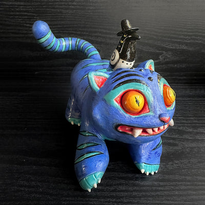 Colorful cat-like figurine with a small figure on its back against a dark background